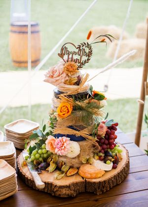 Rustic wedding cake decorated with flowers, fruit, and Mr and Mrs Hunt topper on wooden slice.