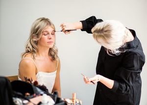 A makeup artist applies eye makeup to a blonde bride during wedding day preparations.