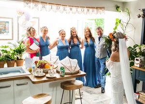 Bride in lace gown photographing bridesmaids in blue dresses with groom under BRIDE LOVE banner.