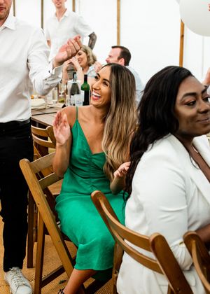 Woman in green dress laughing and clapping at a wedding reception dinner party.