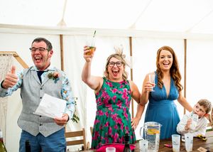 Three happy wedding guests raising glasses in a toast at a marquee celebration.