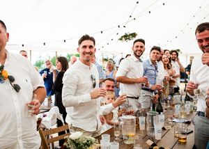 Groomsmen in white shirts laughing and celebrating at a wedding reception tent party.