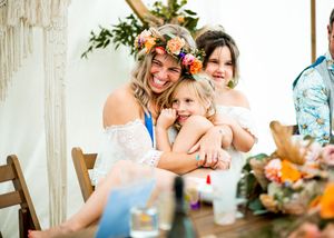 Bride wearing floral crown hugging two young girls at a boho wedding reception.