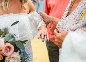 Bride displaying her blue gemstone ring and turquoise nail polish while holding a pastel bouquet at an outdoor wedding.