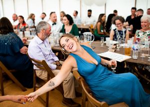 Woman in blue dress laughing and leaning back during wedding reception speeches in a tent.