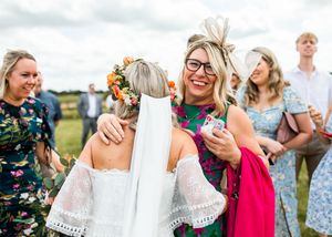 Bride in white lace dress receiving congratulations from smiling guests wearing colorful outfits at an outdoor wedding.
