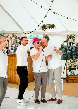 Groomsmen in white shirts singing into microphone during fun wedding reception speeches.