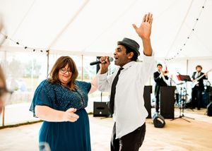 Singer and dancer performing energetically at a wedding reception under a white marquee tent.