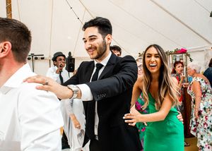 Smiling wedding guests in formal attire dancing and laughing together at a reception party.
