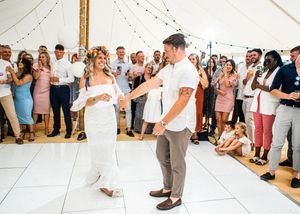 Bride in white dress with flower crown shares first dance with groom before cheering guests.