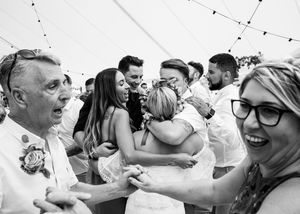 Black and white photo of bride hugging wedding guests joyfully on the dance floor.