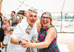 Joyful couple dancing and laughing together at a wedding reception in a sunny marquee.