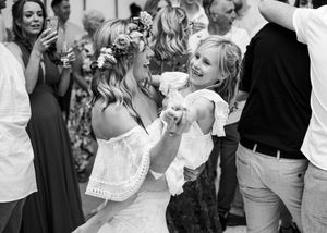 Black and white photo of bride in flower crown dancing with a guest at her wedding.