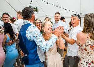 Excited wedding guests clapping and dancing together joyfully inside a bright white marquee tent.
