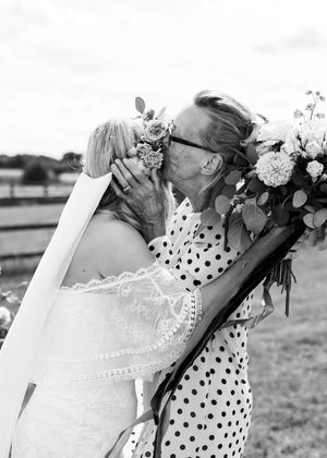 Black and white photo of an elderly woman kissing the bride on the cheek while holding a floral bouquet at a wedding.