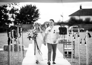 Black and white photo of newlywed couple walking hand in hand down the aisle after their outdoor wedding ceremony.