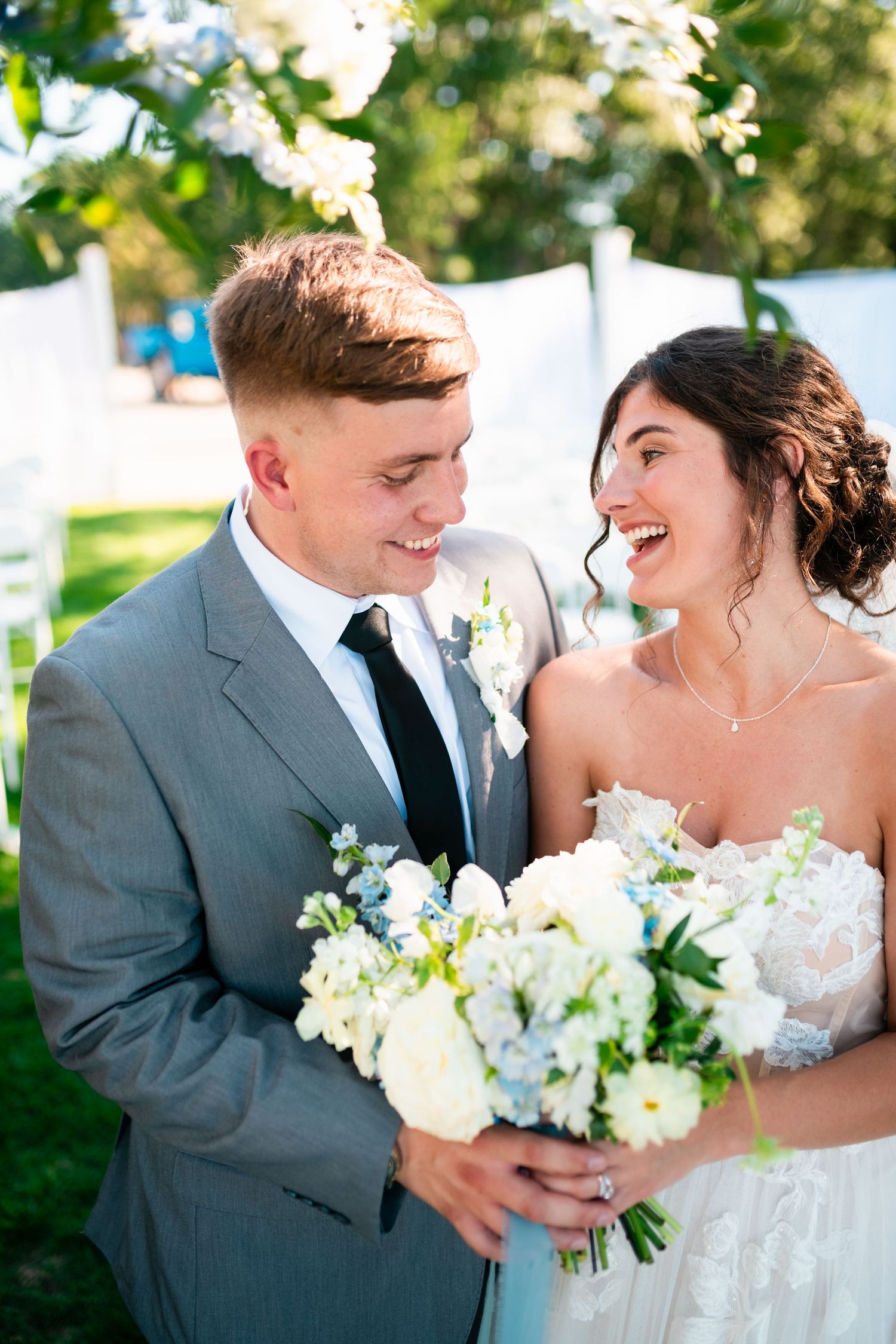 A romantic wedding couple embraces on a lush green lawn during their outdoor celebration at sunset.