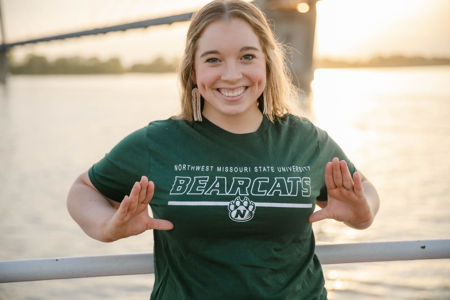 Students in green Bearcats apparel pose at sunset by the water during a golden hour photo session.