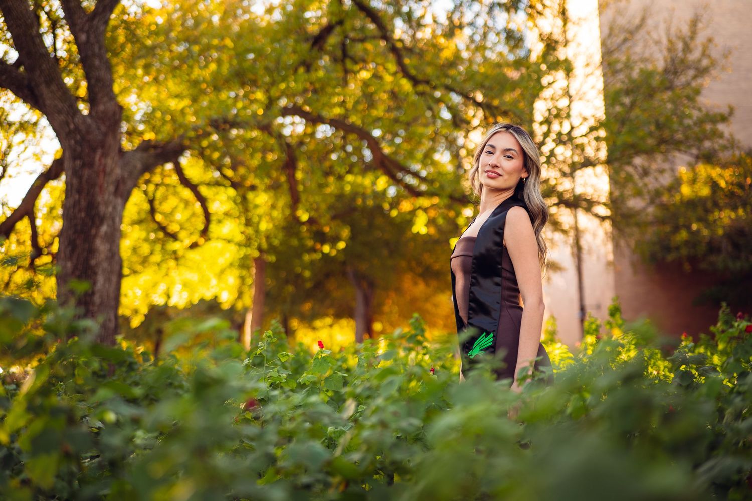 Graduate poses in natural setting with golden sunlight and trees. UNT Graduate Portraits by Eric Aaberg Photography in DFW.