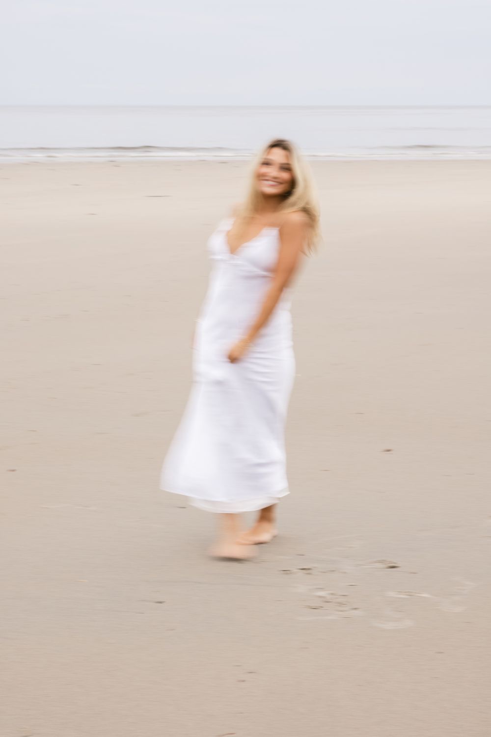 Blond girl wearing a long white maxi dress spins with blurry photo effect for senior photos at North Hampton Beach. York senior photographer