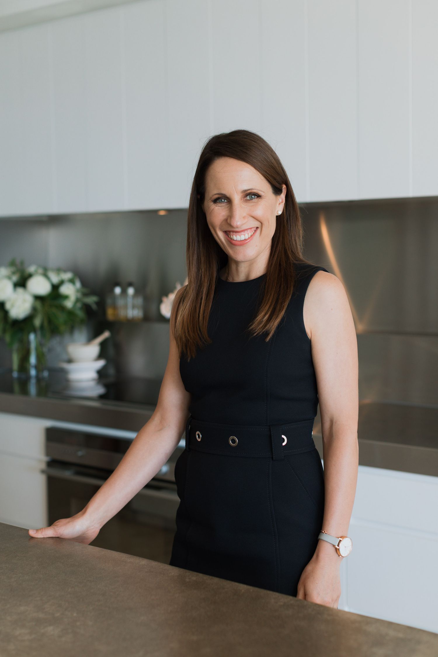 Professional wearing a sleek black sleeveless top sits at modern white desk in contemporary office space.