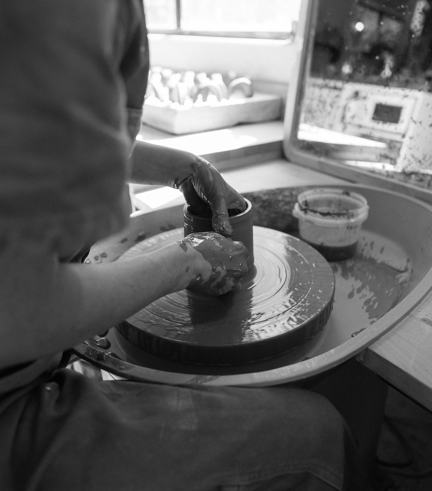Black and white photo of a person shaping clay on a pottery wheel in a studio workshop.