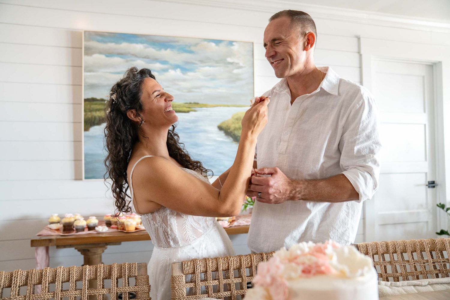 A couple laughs and dances together in a bright indoor setting with a cake nearby.