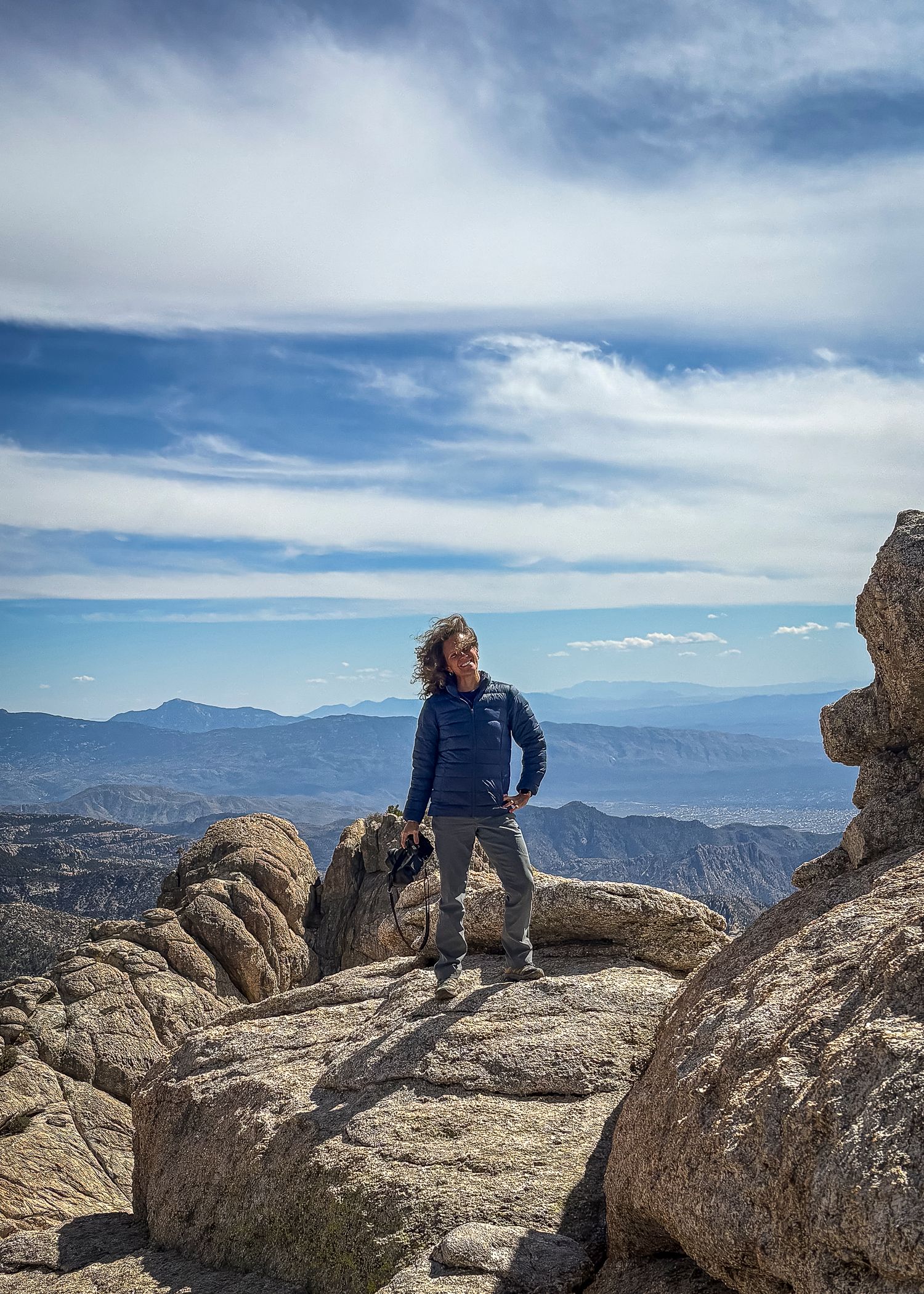 A hiker enjoying the panoramic mountain views while sitting on rocky terrain at high elevation.
