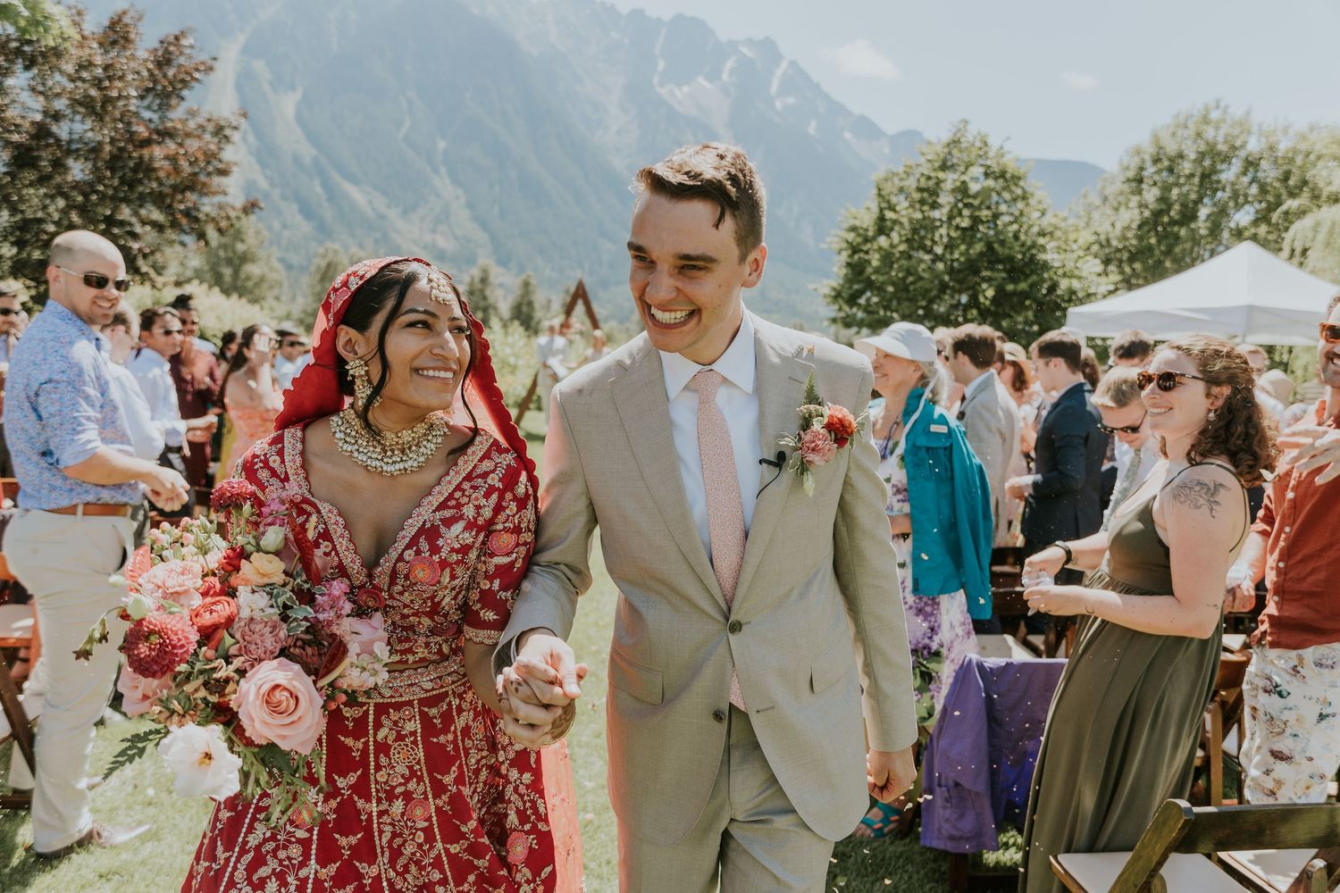 A scenic mountain wedding celebration with guests gathered outdoors on a sunny summer day.