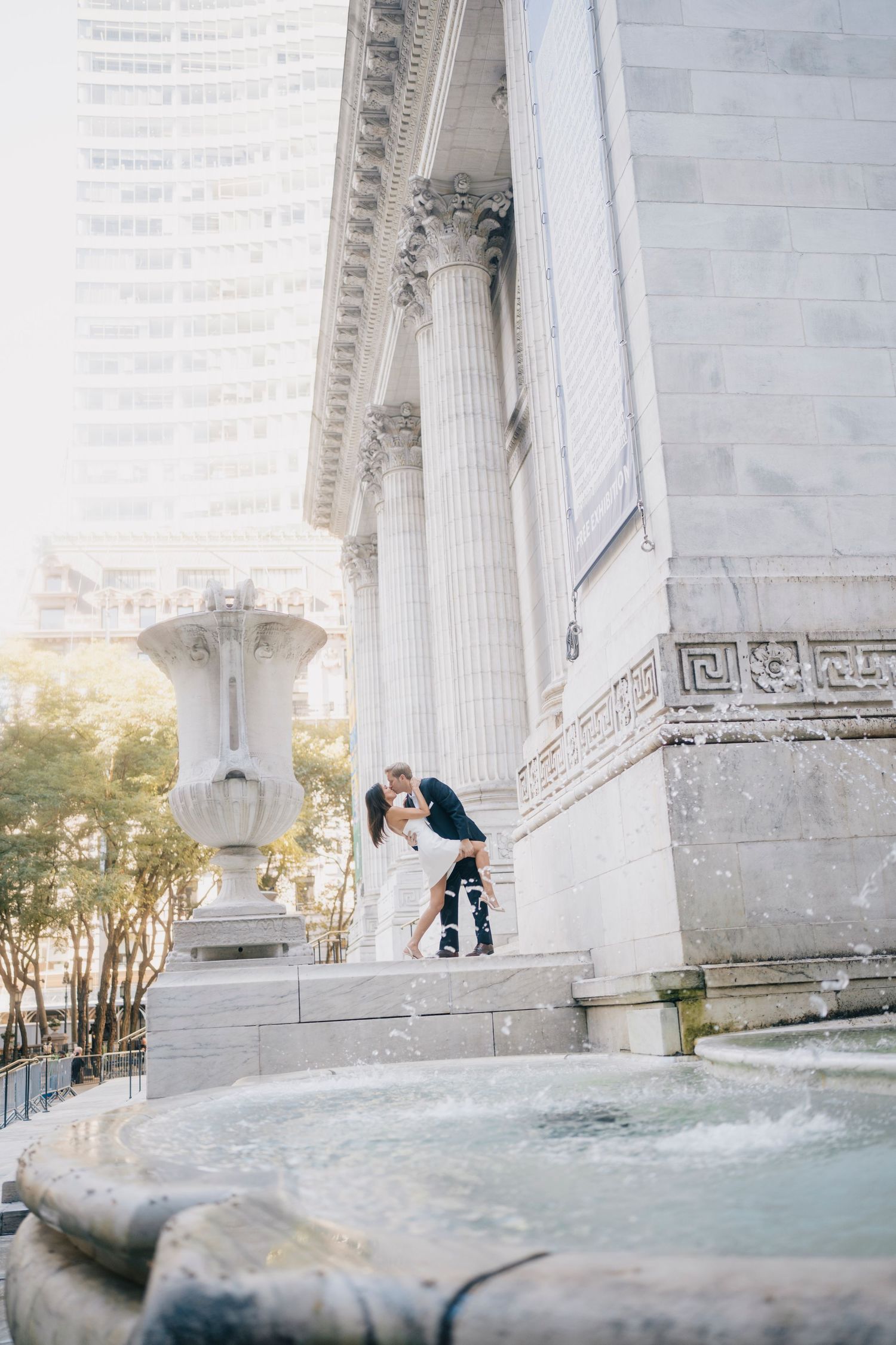 A romantic couple embraces under grand marble columns at the Jefferson Memorial during a bright sunny day.