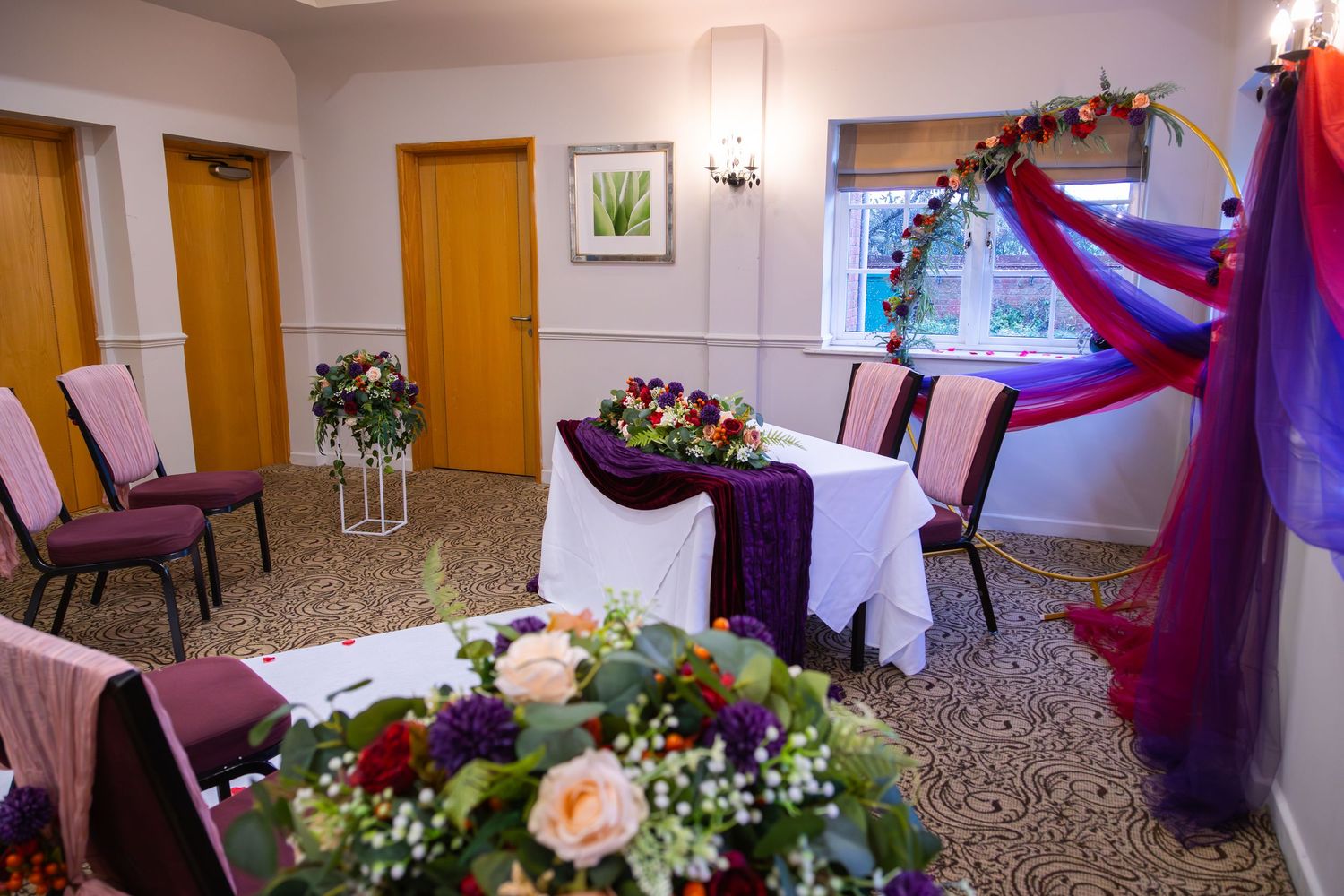 Elegant wedding reception hall decorated with red and purple drapes, white flowers and soft lighting for a romantic atmosphere.