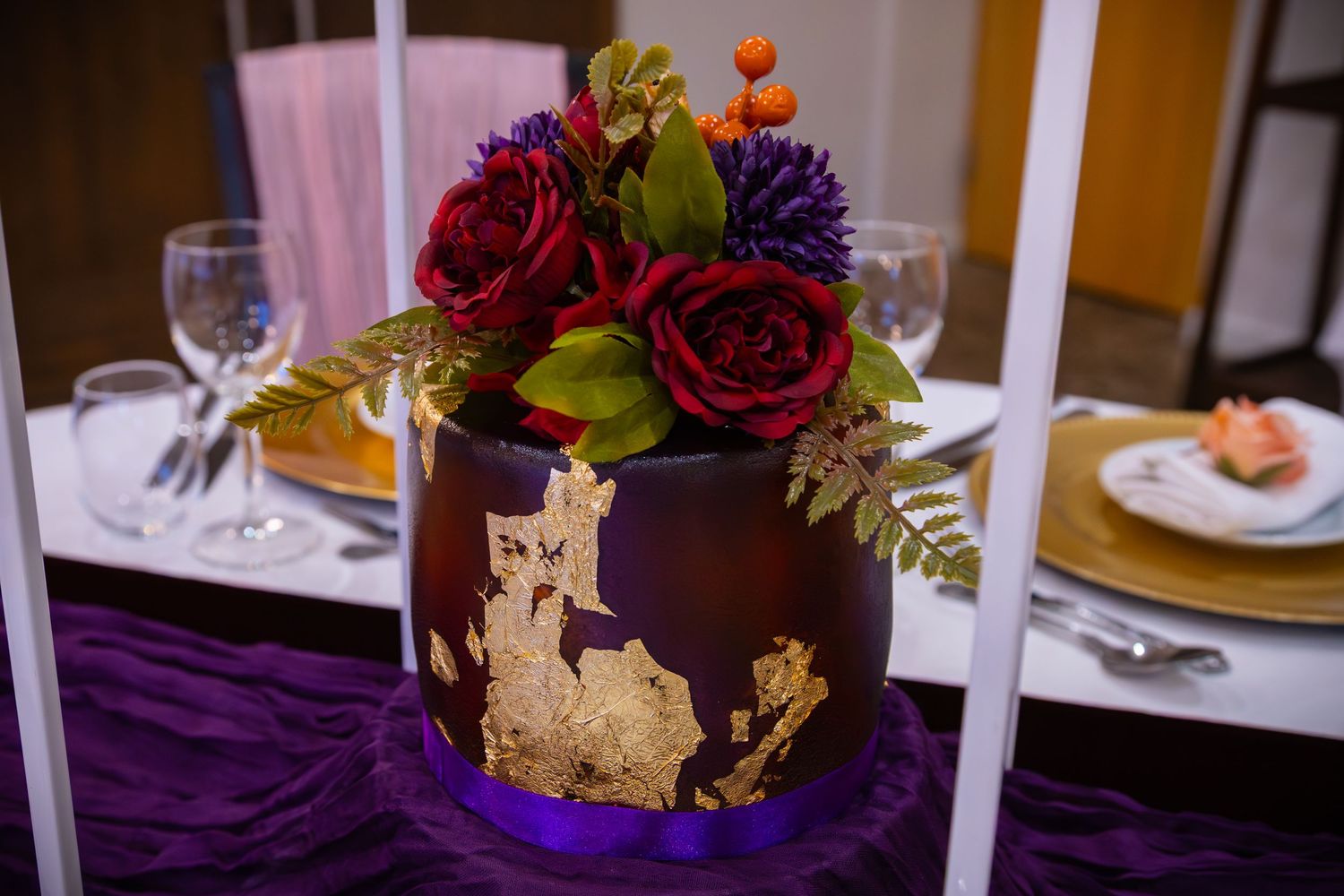 Elegant wedding reception table settings with purple and red floral centerpieces, white candles, and gold accents.