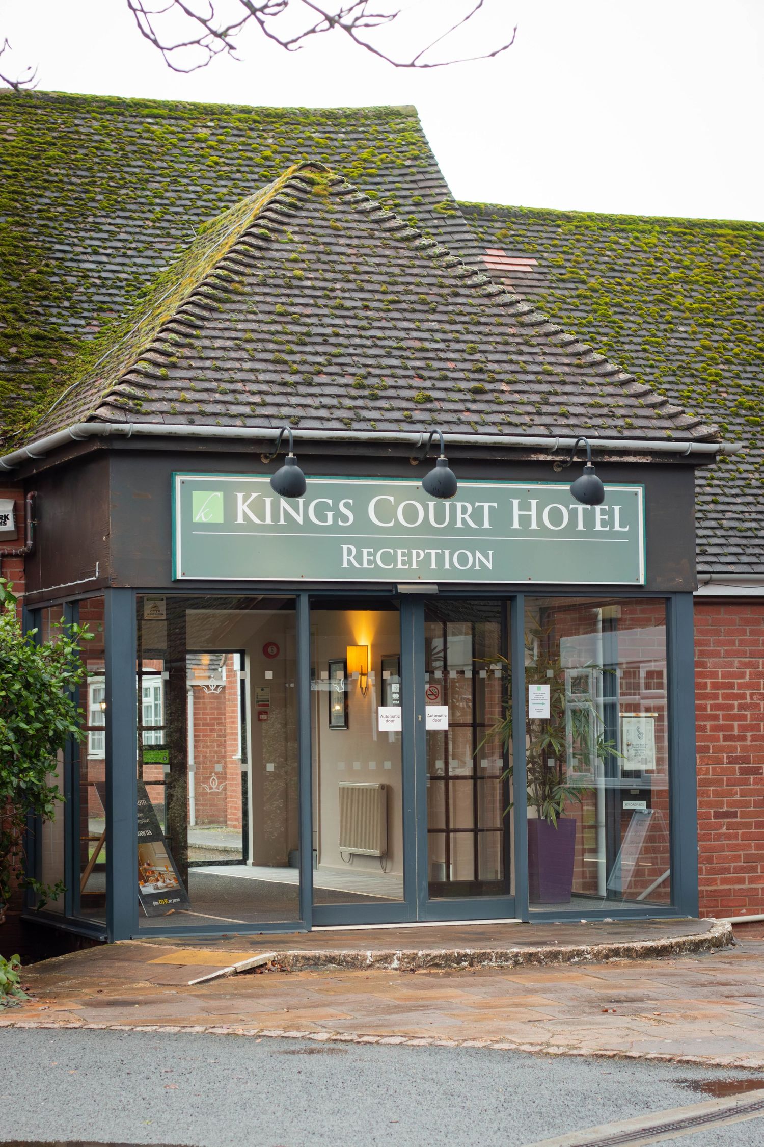 Entrance to Kings Court Hotel reception with moss-covered tiled roof and glass revolving door.