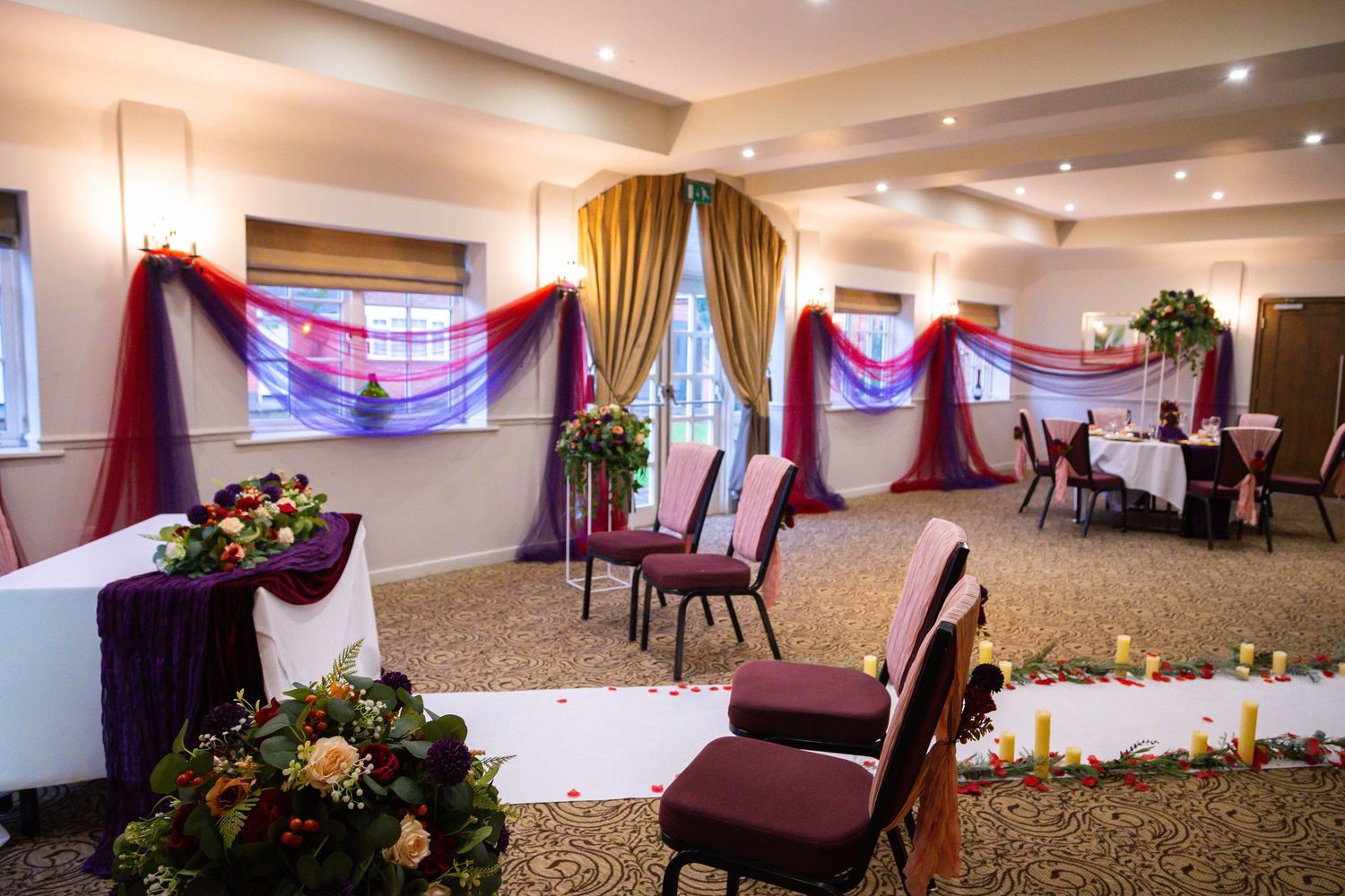 A panoramic view of an elegant banquet hall with burgundy chairs and decorative drapes showcasing event space setup.