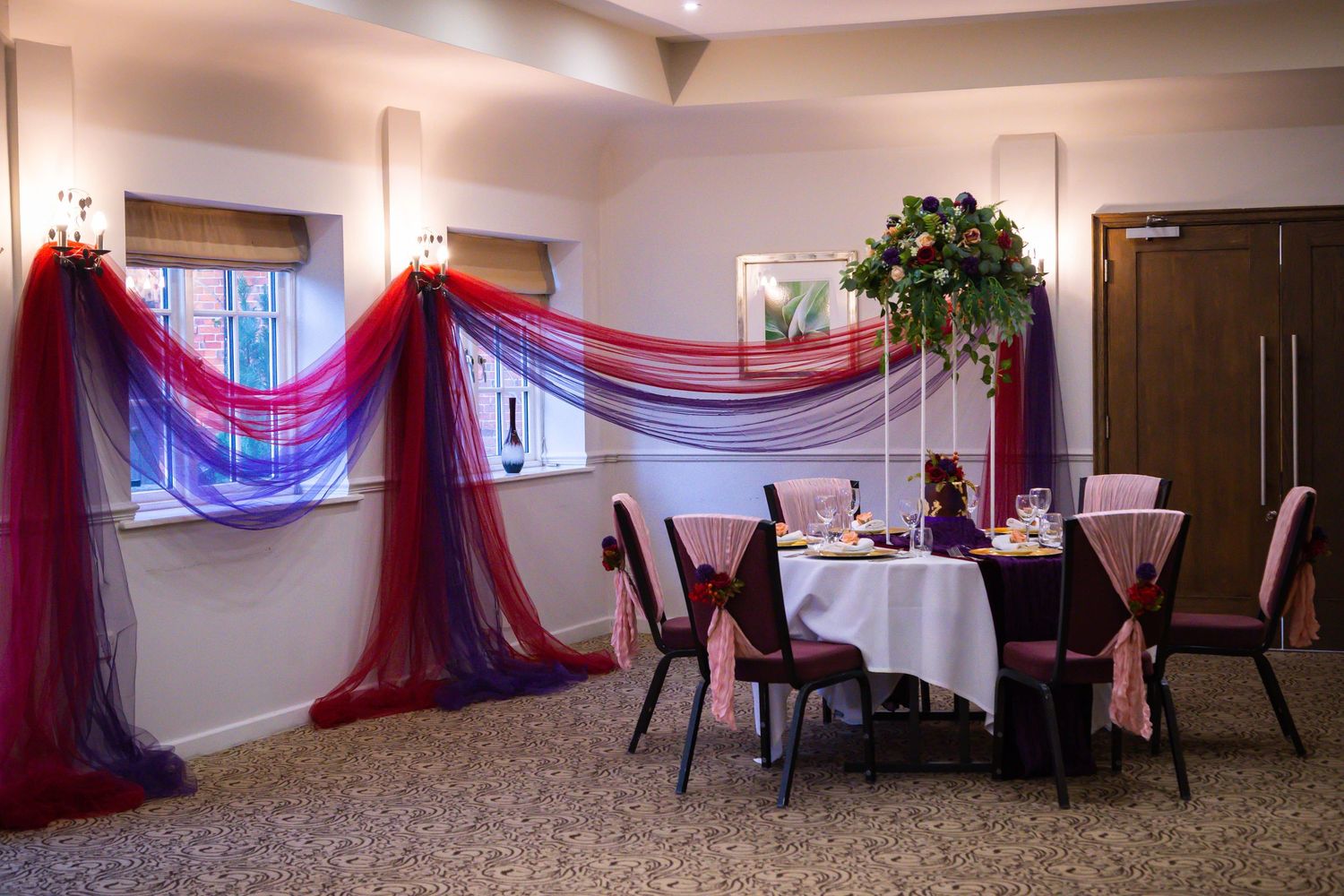 Large banquet hall decorated with red and purple fabric draping and round dining tables set for an event.