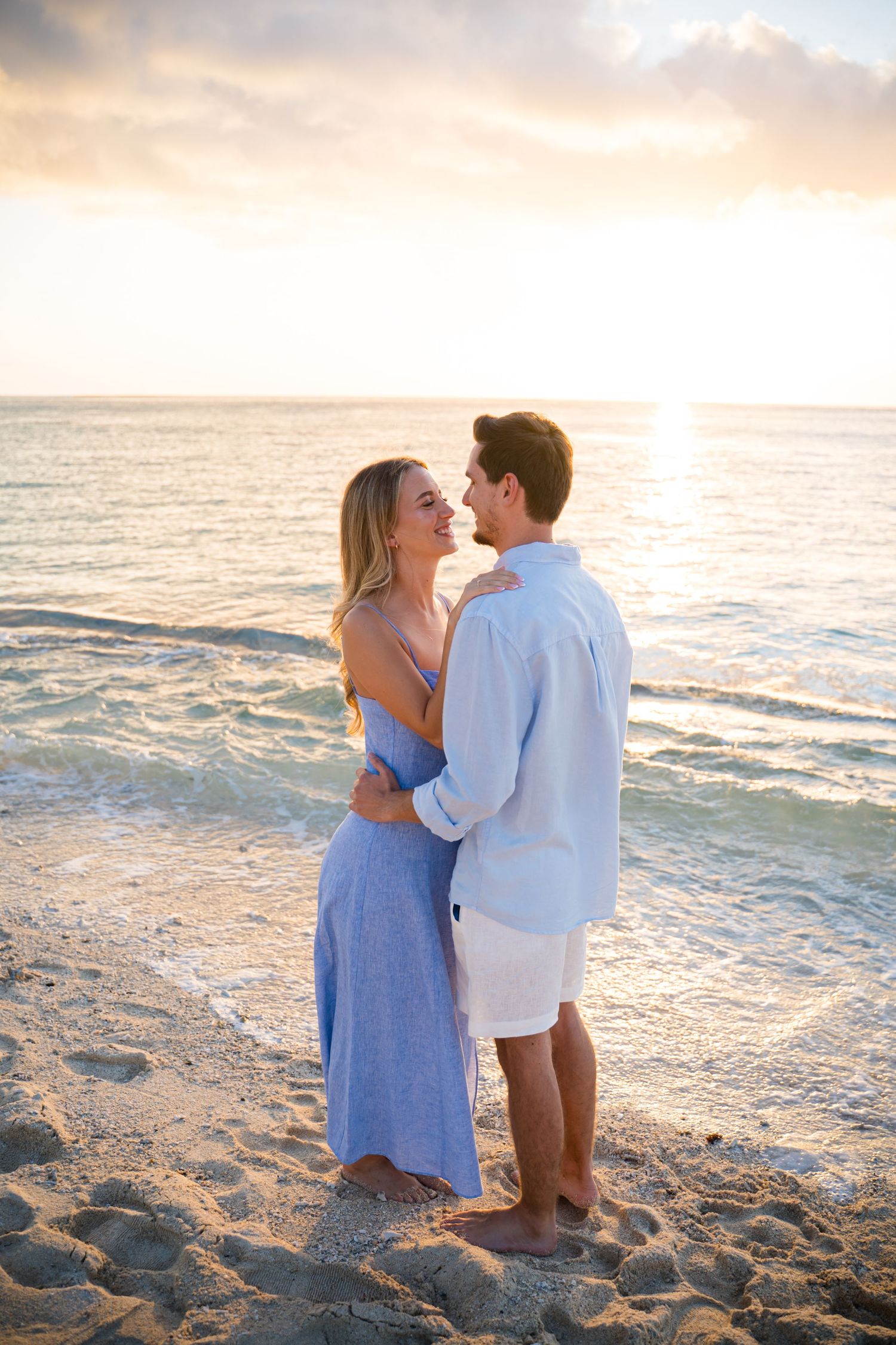 A couple embraces on a sandy beach during golden hour.
