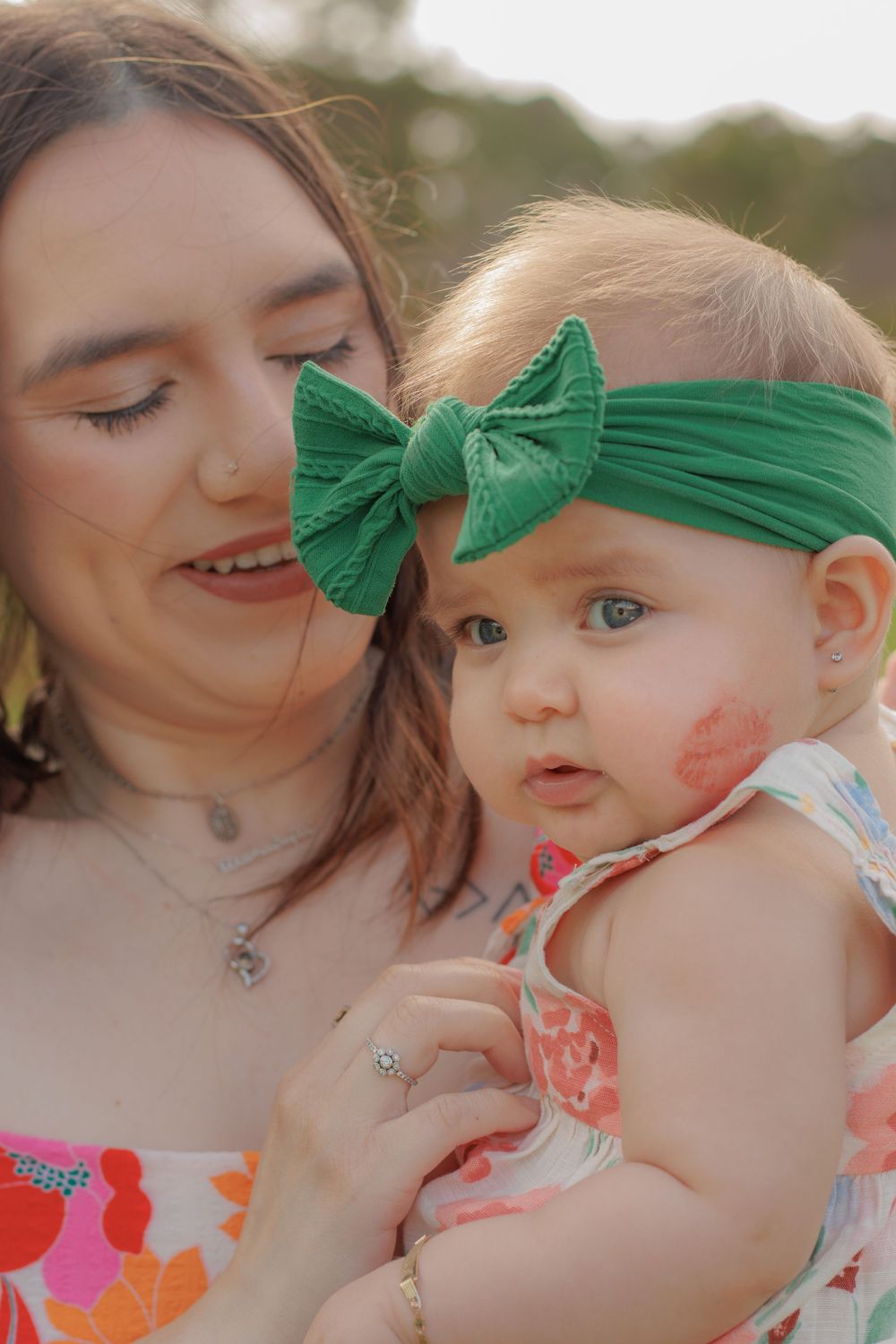 A sweet outdoor portrait featuring a floral dress and green bow headband in warm sunlight.