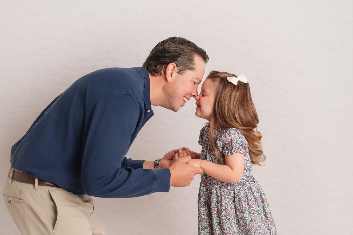 A tender moment between an adult in a navy sweater and a young child wearing a floral dress against a light backdrop.