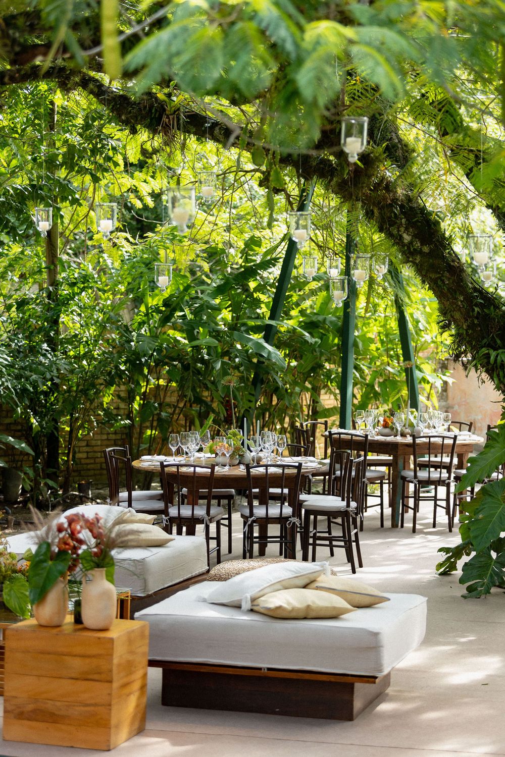 Outdoor restaurant seating area with wooden tables and chairs under lush green trees and natural canopy.