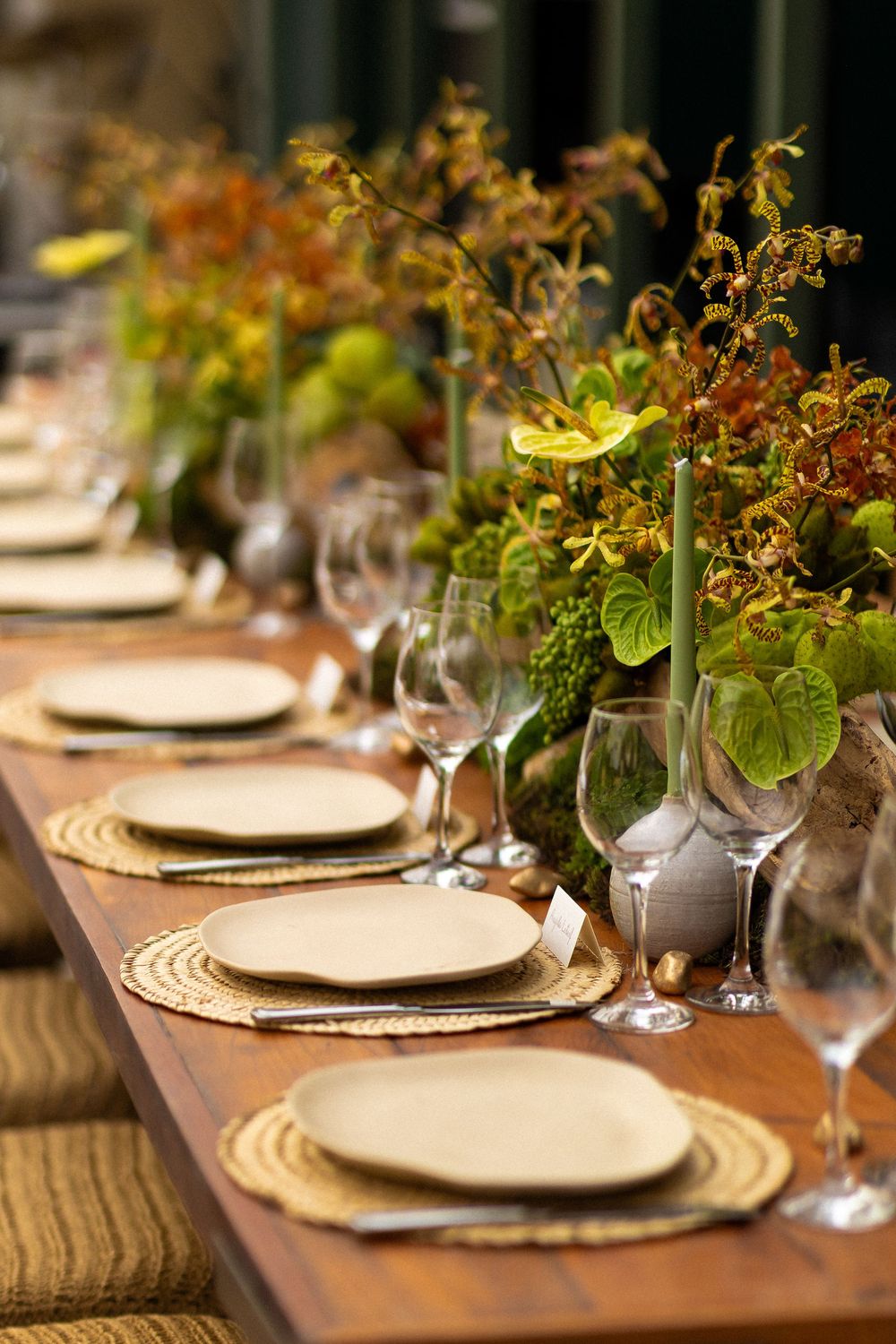 Elegant table setting with white plates and natural greenery centerpieces on a rustic wooden dining table.