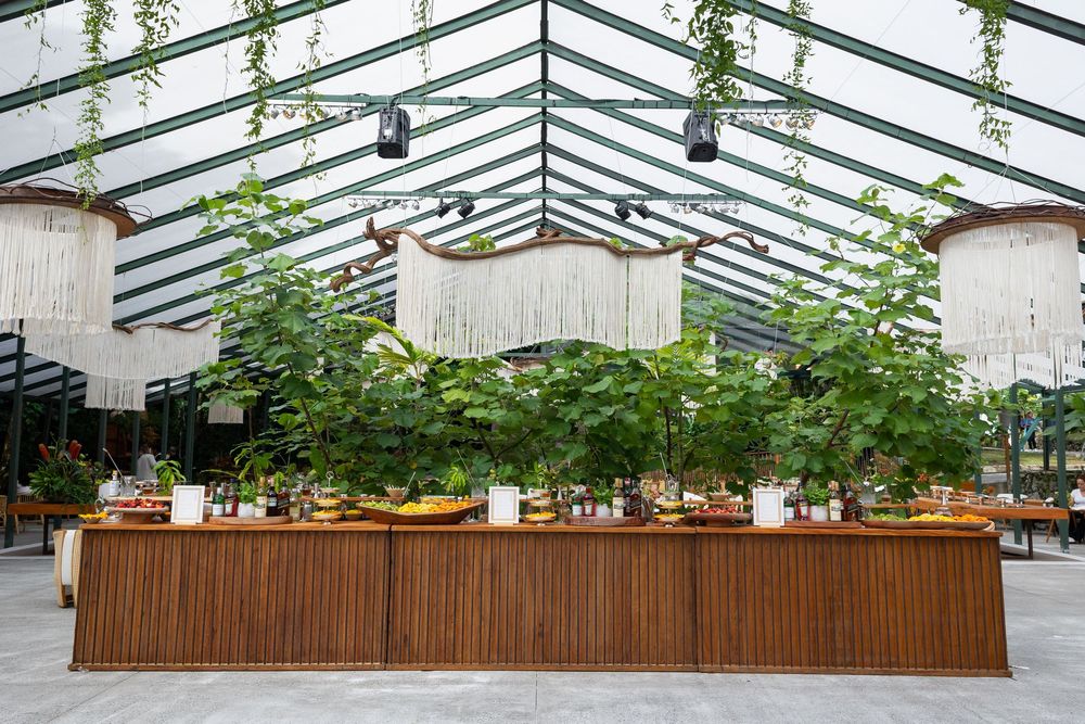 Long wooden planter boxes with small trees and greenery line an outdoor urban plaza area under glass roof panels.
