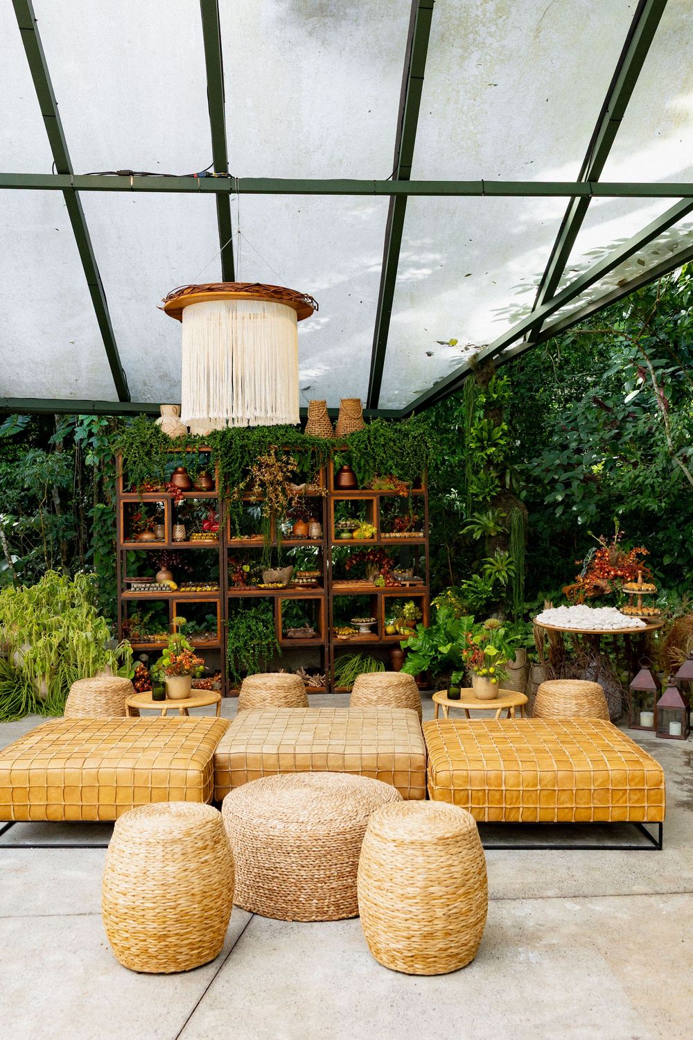 Modern boho lounge area with woven rattan ottomans and wooden shelving displays in a greenhouse-style space.