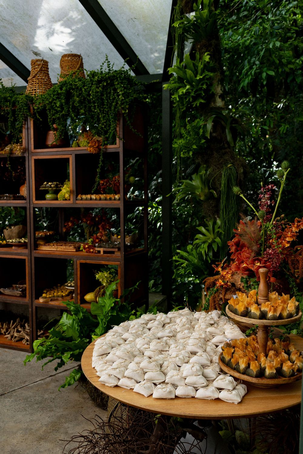 Elegant dessert display with white meringues on a round table and shelving unit filled with treats in a greenhouse setting.