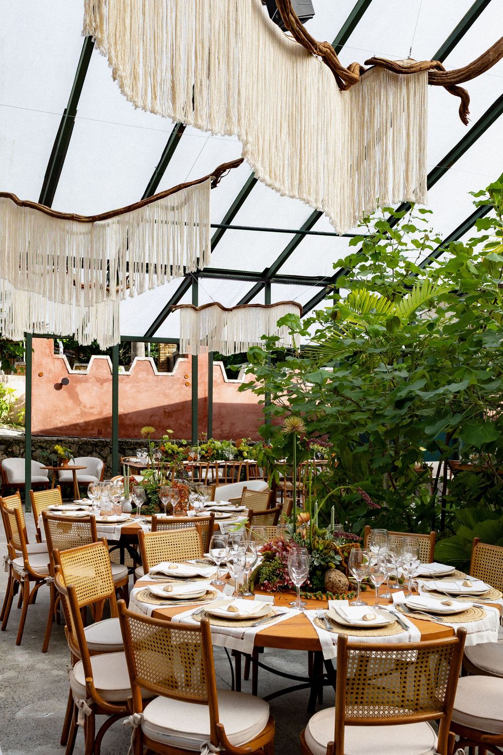 Elegant restaurant interior with cane back dining chairs and hanging pendant lights under a glass ceiling.