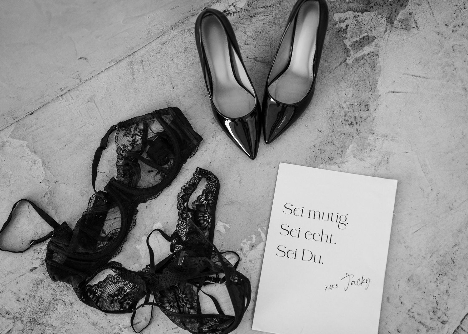 A collection of black high heel shoes arranged artistically on a light marble floor with handwritten notes.