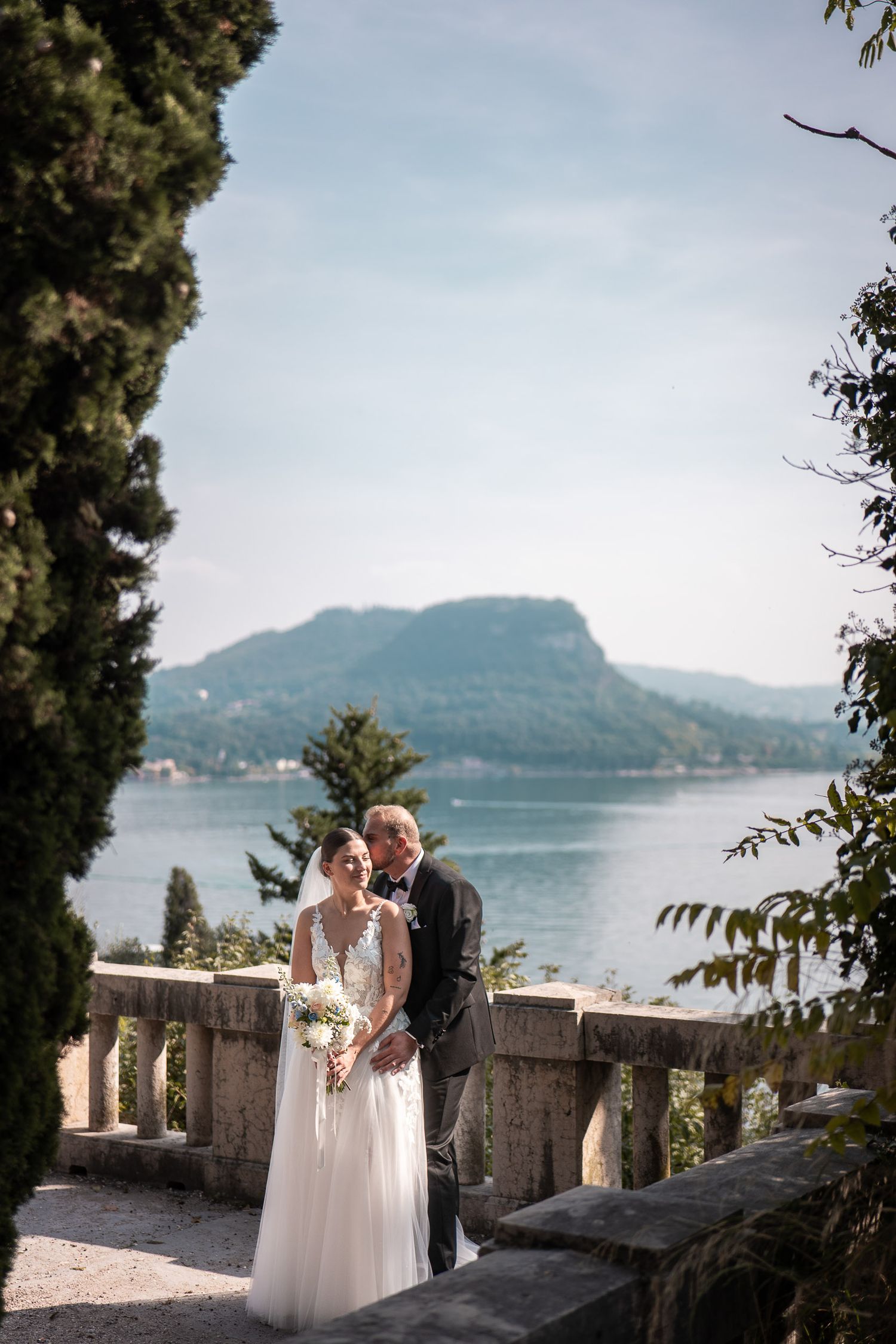 Brautpaar küsst sich auf einer Terrasse mit Panorama-Blick über den Gardasee in Bardolino.