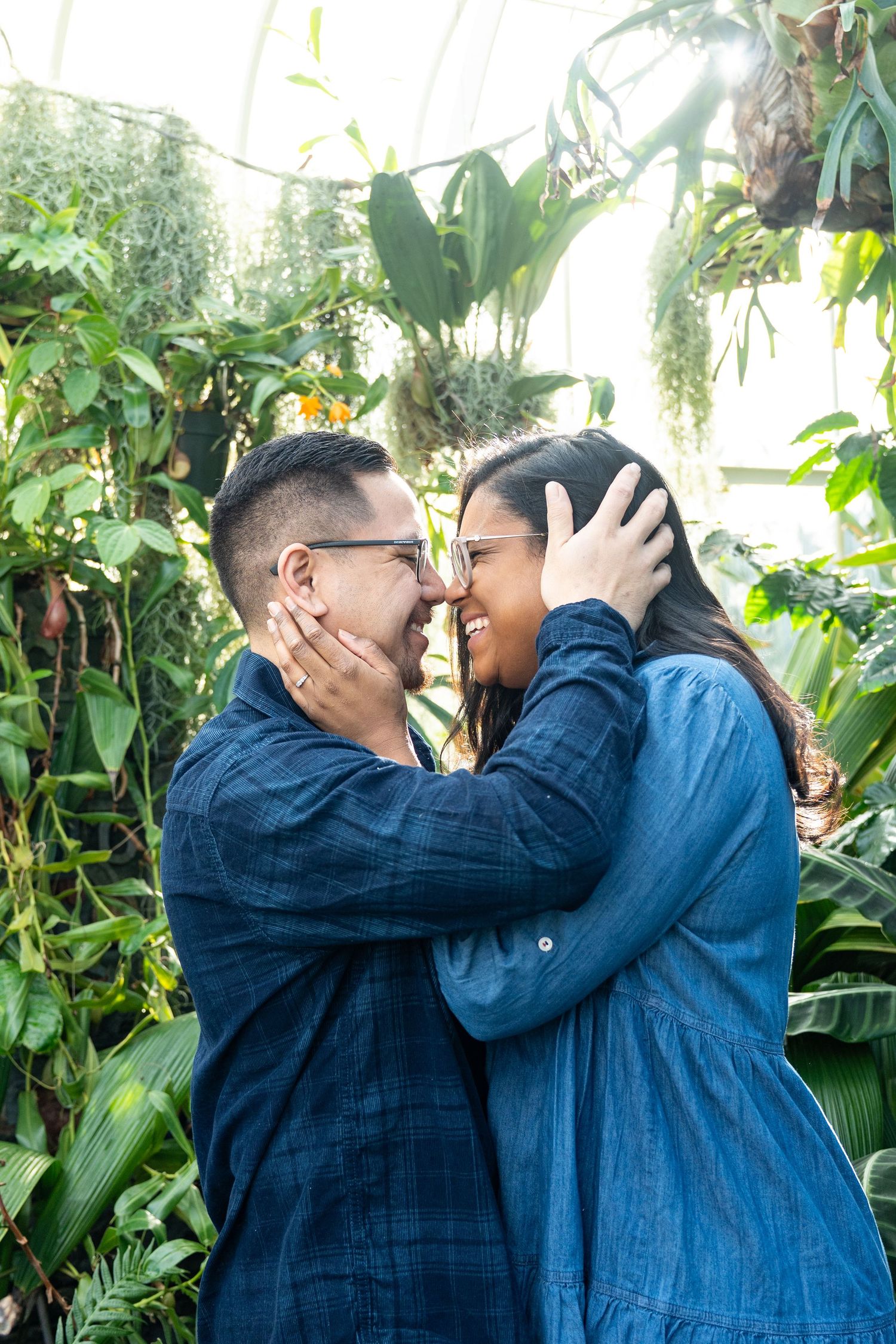 Two people wearing denim embrace each other in a lush tropical garden setting with banana plants in the background.