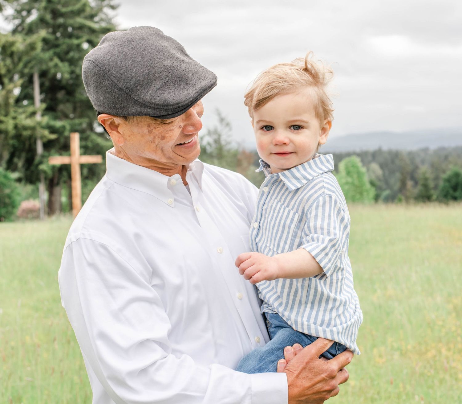 Parent and child share a tender moment in a grassy field while wearing coordinating white and blue outfits.
