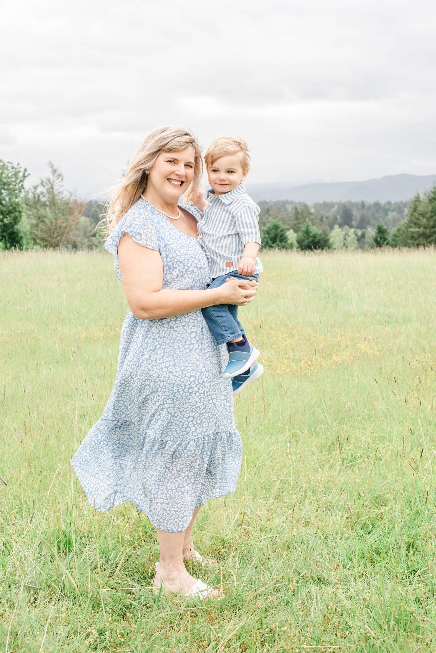 A parent and child share a joyful moment together in a grassy meadow with mountains in the background.