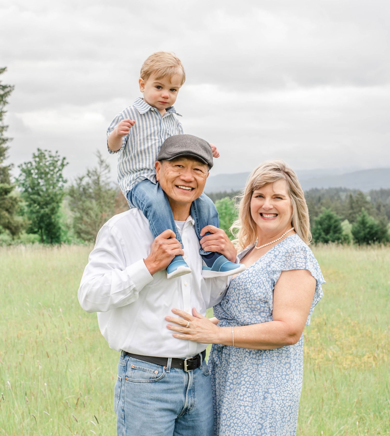 A couple and child share joyful moments together in a sunny meadow wearing coordinated blue and white outfits.